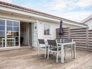 A patio with a table and chairs, a wooden deck, and a building with a tiled roof and a sliding glass door. - 4 Person Holiday Home in Laeso (Læsø)