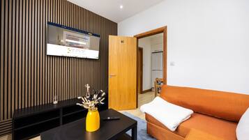 A modern living room with a flat-screen TV mounted on a wooden wall, a sofa, a coffee table, and a door leading to another room.