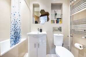 A modern bathroom with a white sink, toilet, and shower area. - West Kensington 2BR | 1-Min Tube | Heathrow Direct (Greater London)