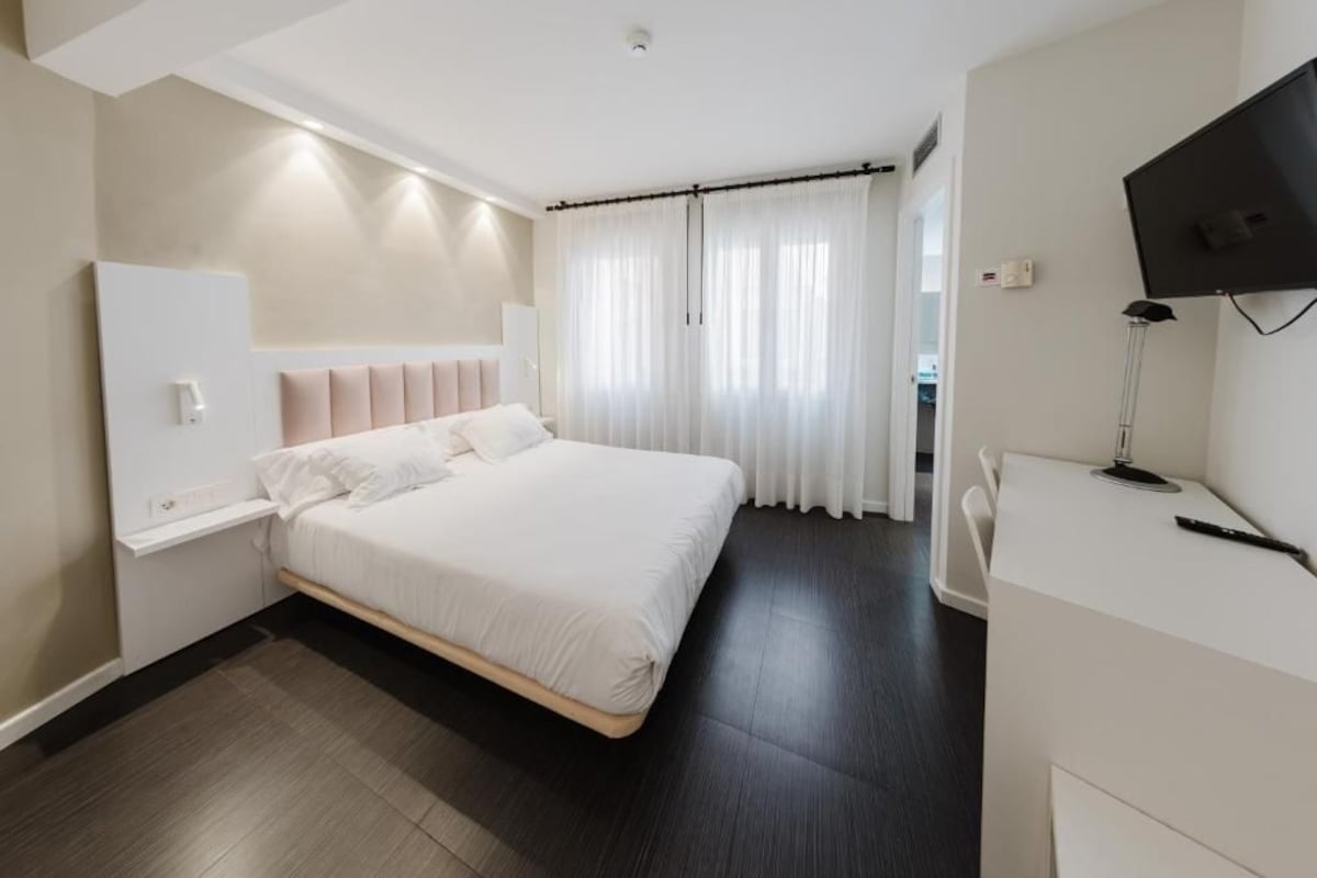 Una camera d'hotel moderna con un letto grande, una TV a schermo piatto e una scrivania con una lampada.