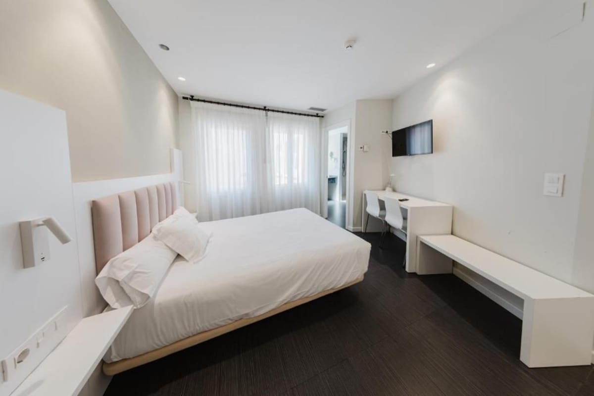 Una camera da letto moderna con un letto, un comodino, una panca e una TV a parete.