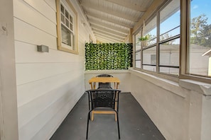 A narrow corridor with a wooden table and a chair, a green leafy wall, and windows with a view of the outside. - Cincy 5BR Escape Zoo Xavier Sleeps 7 (Cincinnati)