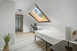 A modern bedroom with a slanted ceiling skylight, a bed, a desk, and a potted plant. - Cincy 5BR Escape Zoo Xavier Sleeps 7 (Cincinnati)