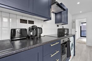 A modern kitchen with dark cabinets, a coffee maker, a toaster, and a microwave. - Luxury Suite with Private Balcony - Edgware Rd (London)