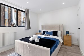 A modern bedroom with a bed, bedside tables, and a window with a view of buildings. - Luxury Suite with Private Balcony - Edgware Rd (London)