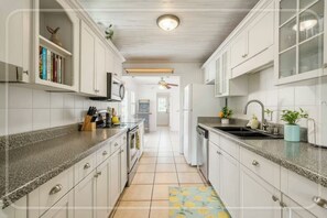 A kitchen with white cabinets, granite countertops, a microwave, and a ceiling fan. - 3-BR Beach House in enchanting St. Petersburg Pool, Grill & More (St. Petersburg)