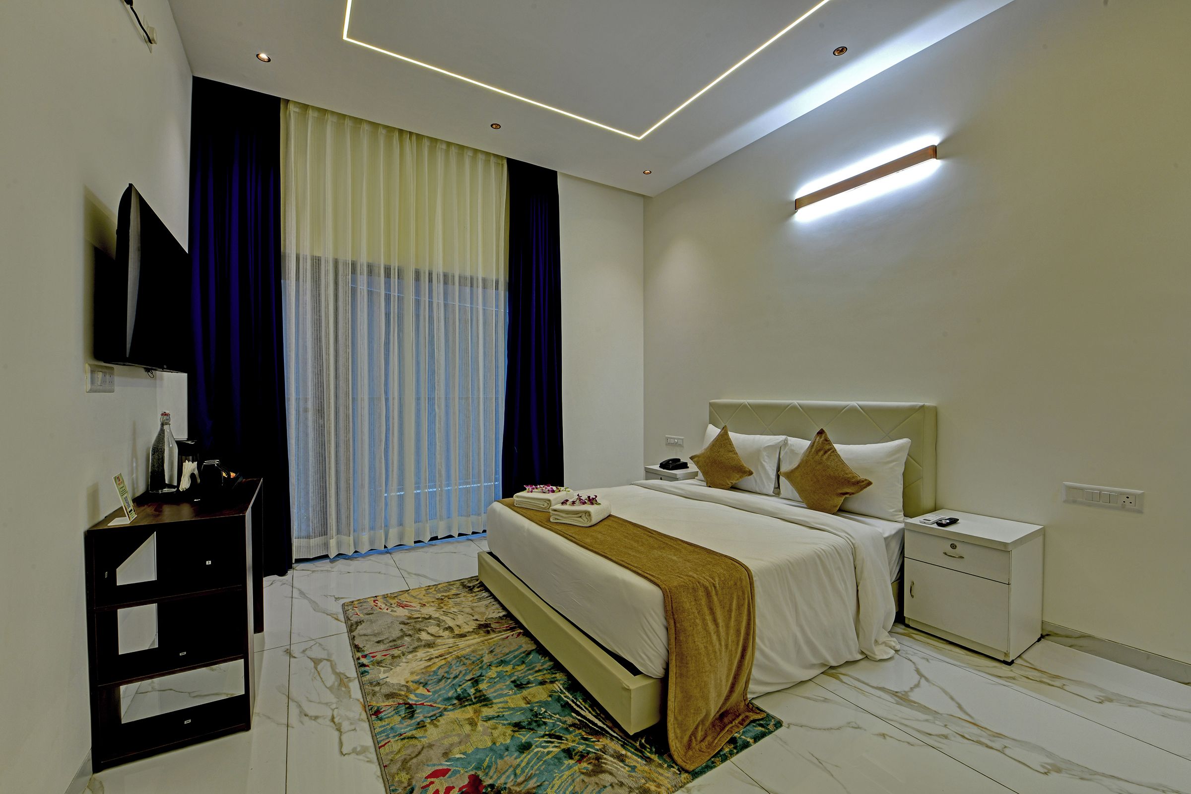 A modern hotel room with a bed, bedside table, and a TV mounted on the wall.