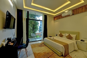 Habitación de hotel con cama, mesita de noche y escritorio con silla. Hay un balcón con vistas a zonas verdes.