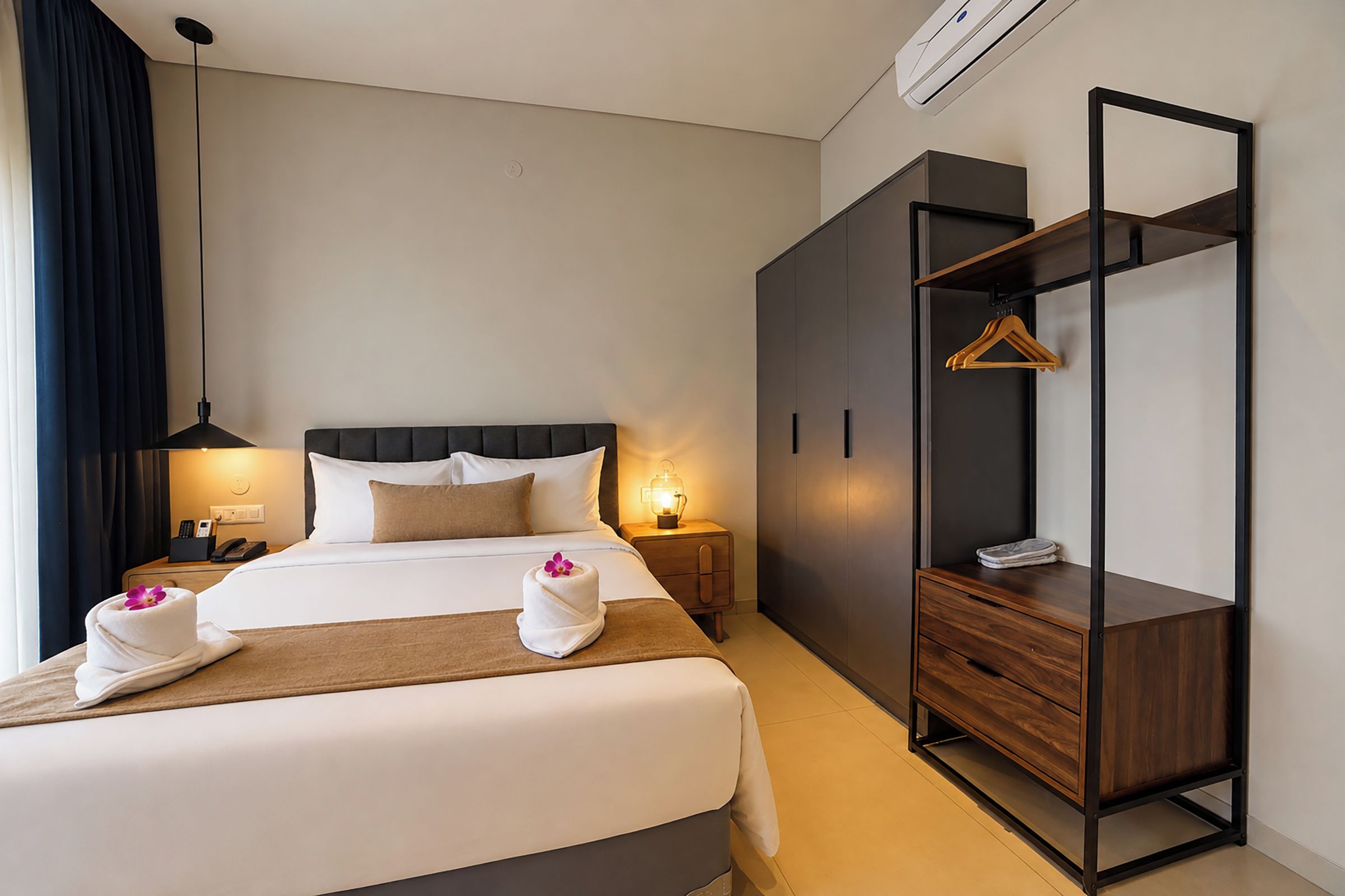 Una habitación de hotel con una cama, mesitas de noche, un armario y un ropero.