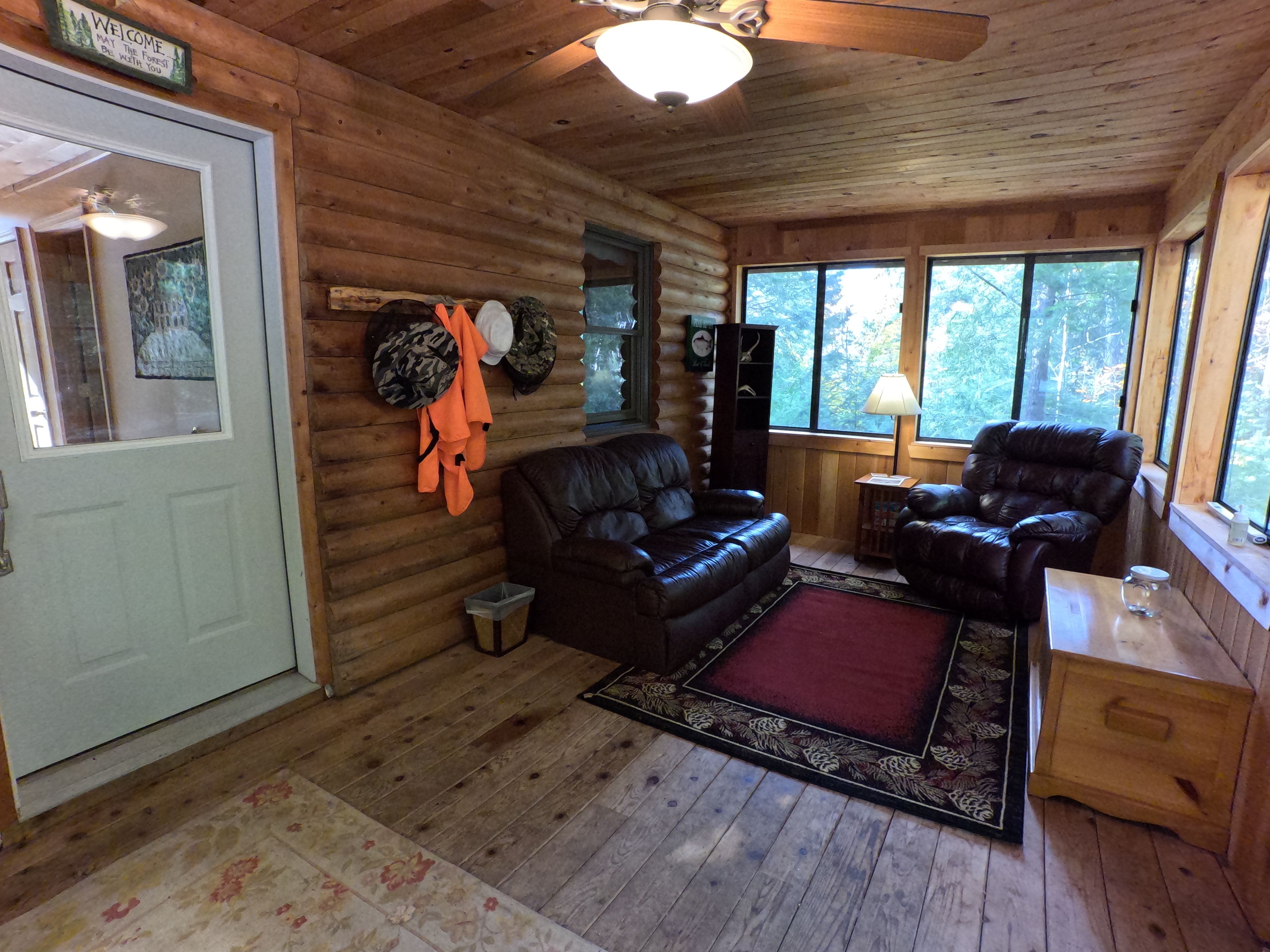 A log cabin interior with a leather sofa, a red rug, and a leather armchair.