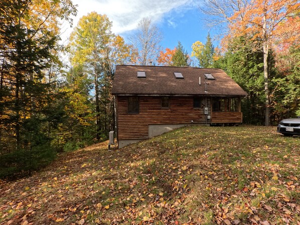 A log cabin with a sloped roof, a small porch, and a car parked nearby.