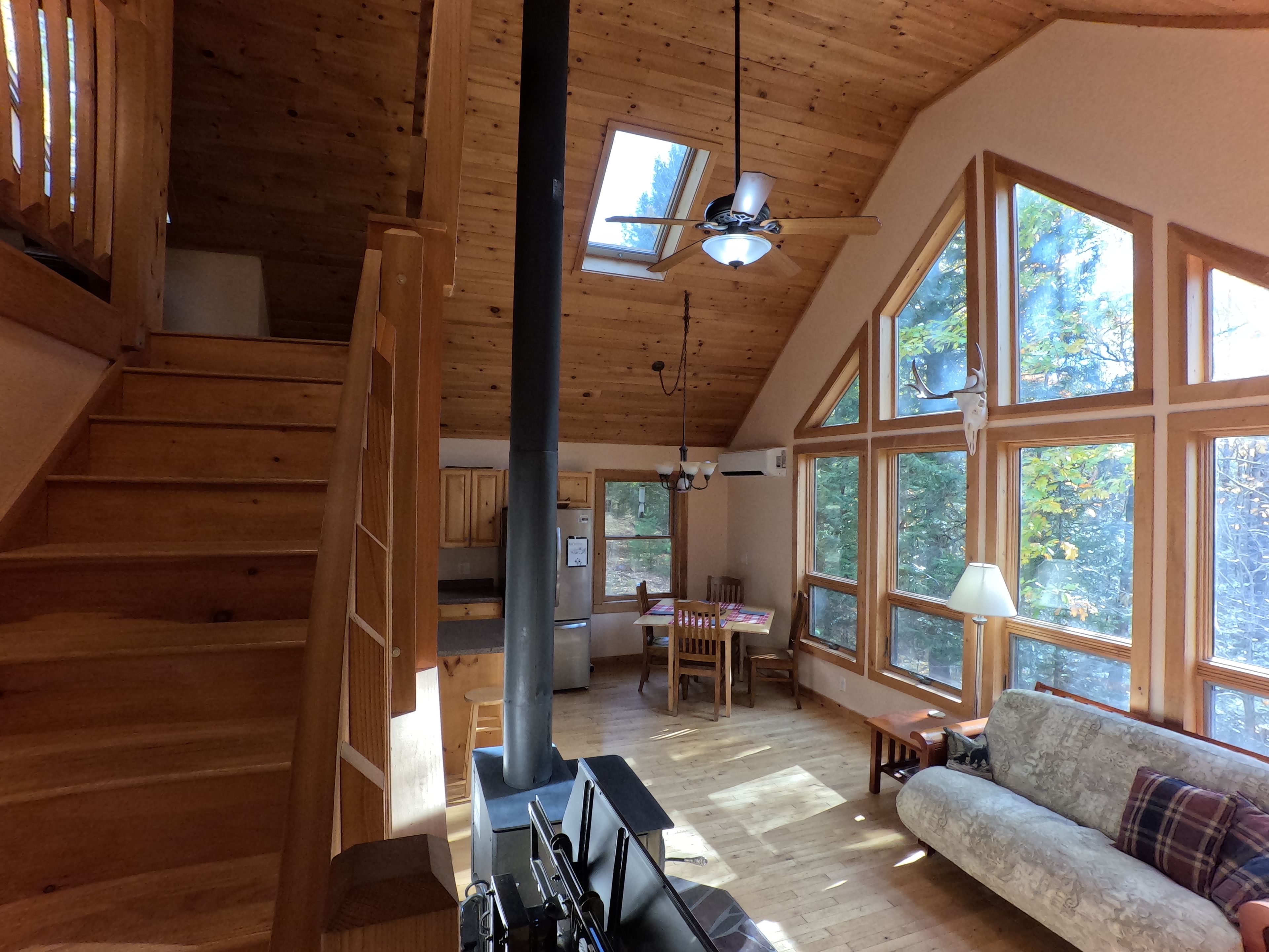 A spacious wooden interior with a staircase, a dining area, and large windows.