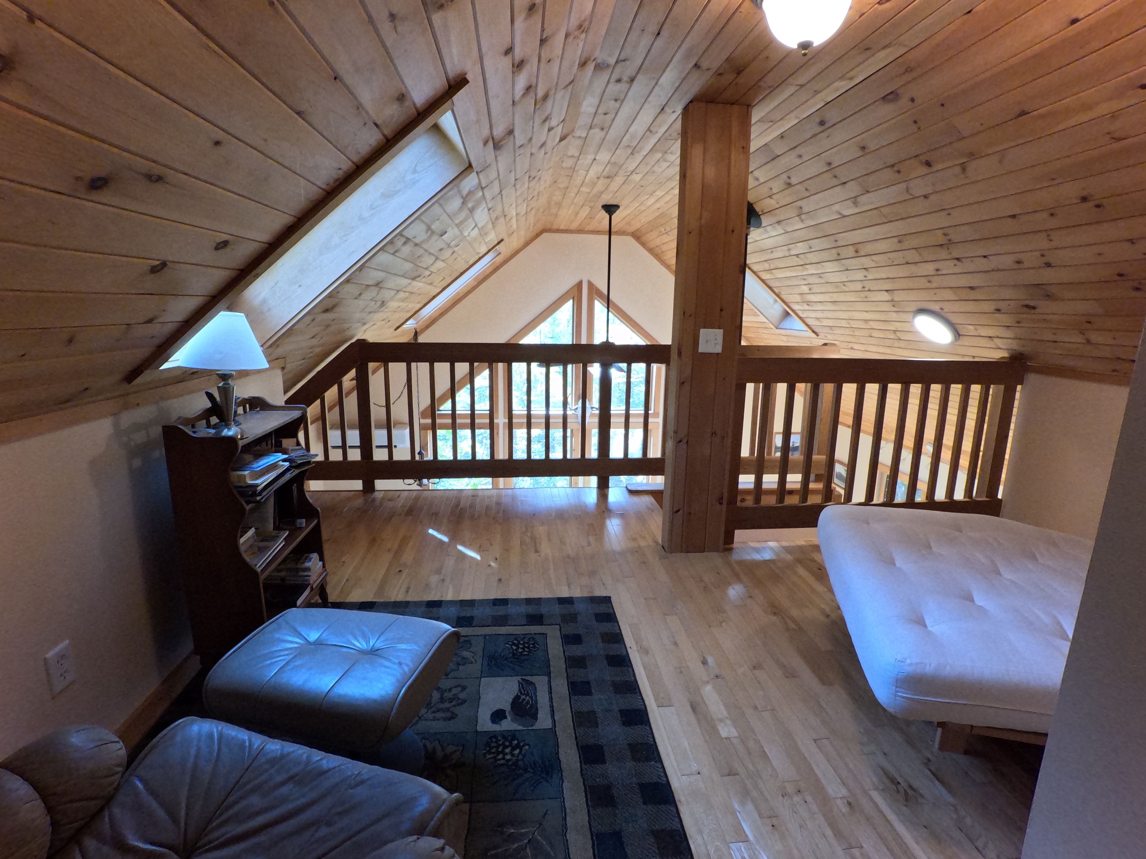 Une chambre à coucher de style loft avec un plafond en bois, un lit, un bureau avec une lampe et une vue sur l’extérieur.