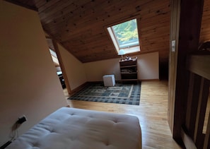 A room with a sloped ceiling, a window, a radiator, a sofa, and a wooden floor. - Secluded 2BR Log Cabin On 52 Wooded Acres (Norway)