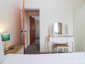A bedroom with a bed, a bedside table, a lamp, a dresser with a mirror, and a door leading to another room. - Bramble (Cleator)