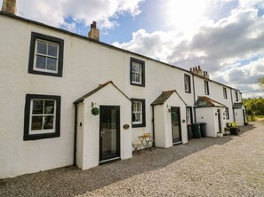 A row of white buildings with black-framed windows and doors, a gravel driveway, and a clear sky. - Bramble (Cleator)