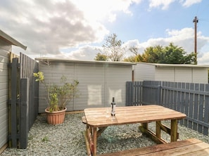 An outdoor patio area with a wooden table and a potted plant. - Acorn (Cleator)