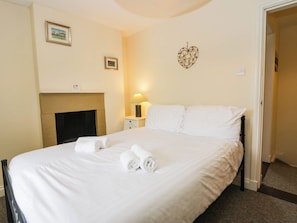 A hotel room with a bed, a nightstand, a lamp, a fireplace, and a wall decoration. - Acorn (Cleator)