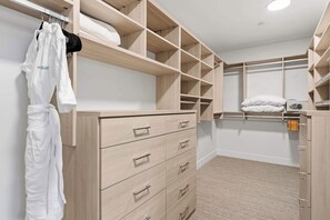 Ein begehbarer Kleiderschrank mit offenen Regalen, eine Einbauschränke mit Schubladen sowie ein Bett mit weißer Matratze und Kissen.