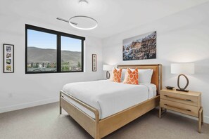 Ein Schlafzimmer mit Bett, Nachttisch, Lampe, Fenster mit Blick und einem Bild an der Wand.