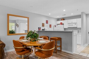 A modern kitchen with white cabinets, a central island, and a dining area with a wooden table and brown chairs. - Spring Creek Getaway (Branson)