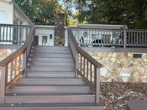 Una escalera de madera con un muro de piedra a un lado y una terraza de madera al otro, que conduce a la entrada de un edificio.