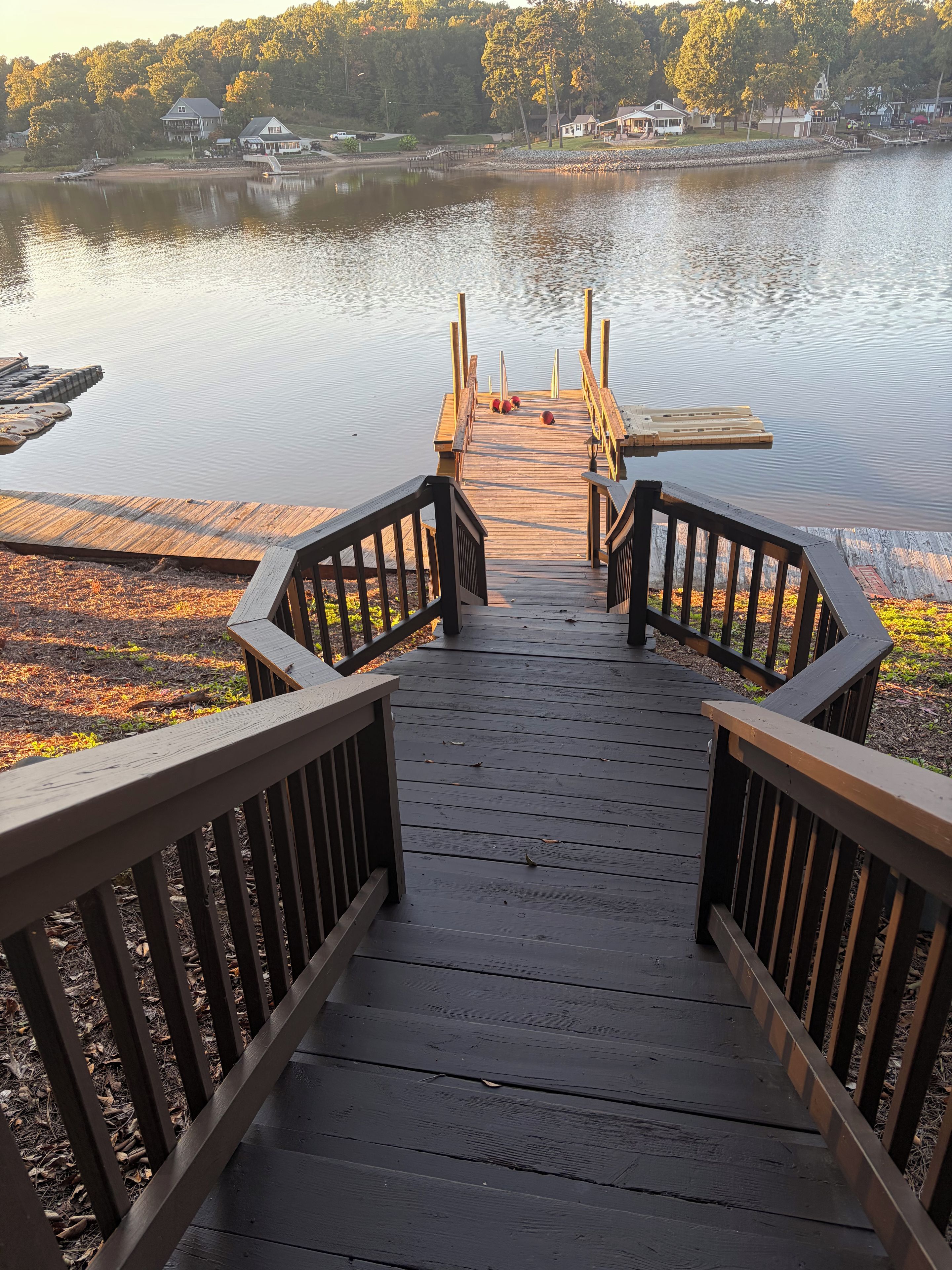 A wooden dock leading to a calm lake with a view of houses in the background.