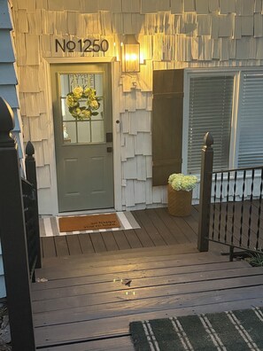 A wooden house entrance with a number sign, a door with a glass panel, a doormat, and a small potted plant. - The Landing at High Rock Lake-Lakefront-Private Dock-Sleeps 9 (Lexington)