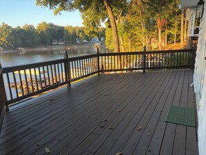 A wooden deck with a railing overlooking a body of water, trees, and buildings in the background. - The Landing at High Rock Lake-Lakefront-Private Dock-Sleeps 9 (Lexington)