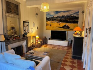 Een woonkamer met een open haard, een grote flatscreen-tv, een hangend schilderij en een geruite vloer.