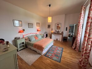 Een slaapkamer met een bed, nachtkastjes, een kaptafel, een spiegel, een open haard en uitzicht op de aangrenzende kamer.