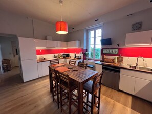 A modern kitchen with a dining area, white cabinets, a red accent wall, and a window providing natural light. - Christmas by the fireplace, elegant 18th-century home, sleeps 12, near St-Émilion (Ruch)