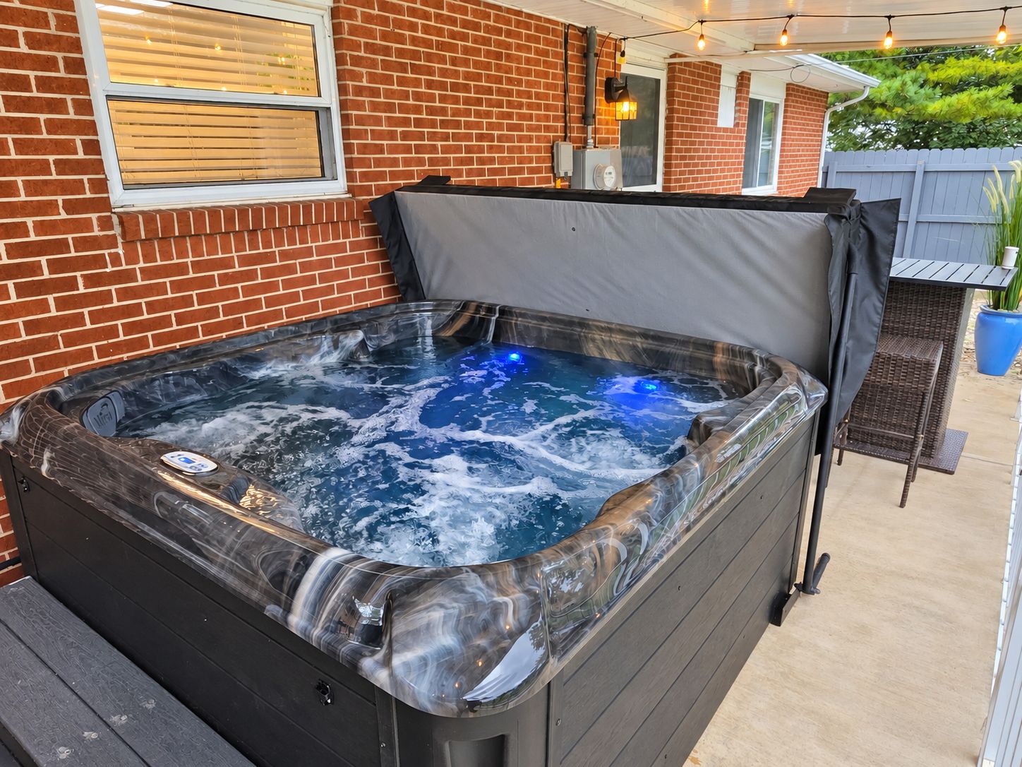 A hot tub with a cover, a brick wall, and a wooden deck.