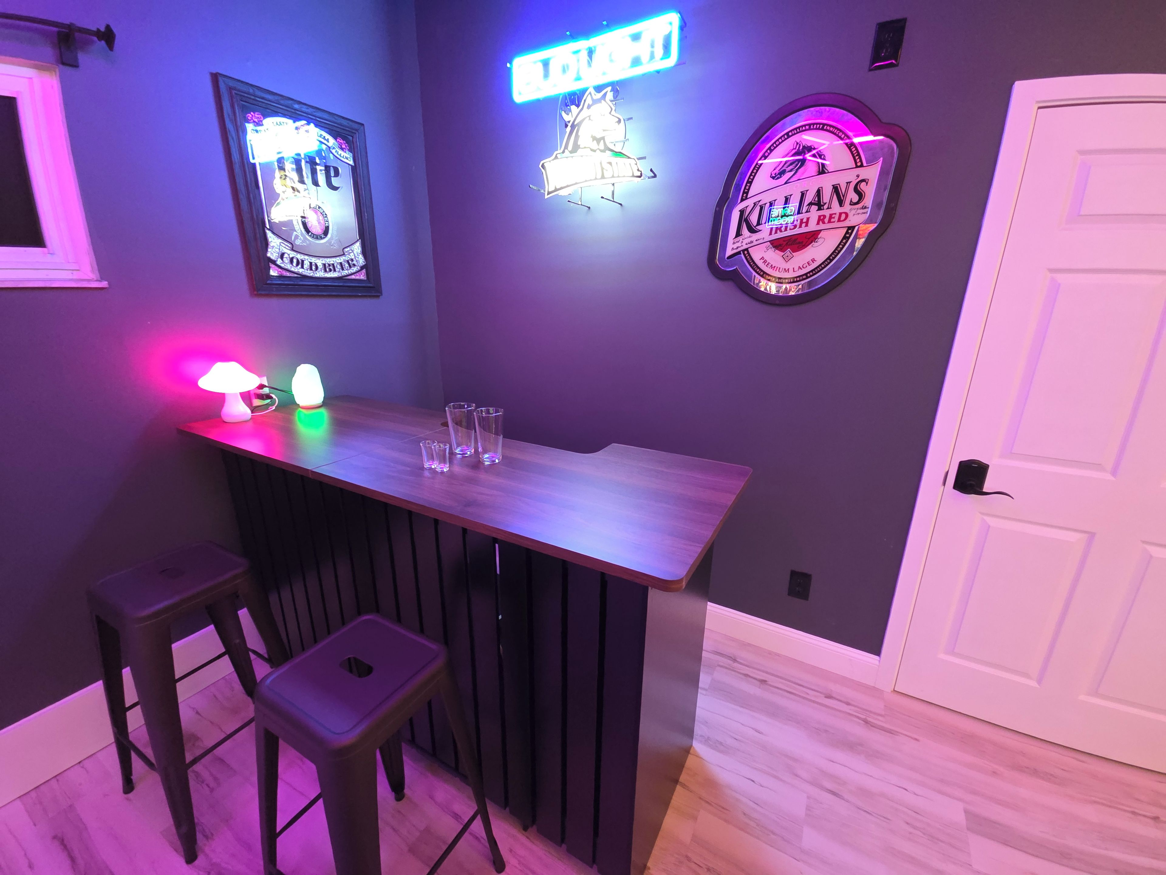 En bar med barstole, et neonskilt og et indrammet logo på væggen.