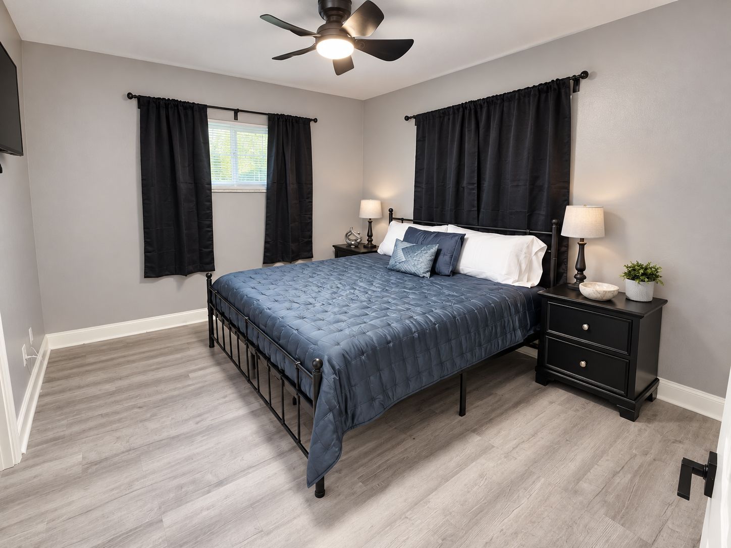 A bedroom with a bed, two bedside tables, a ceiling fan, and a window with curtains.