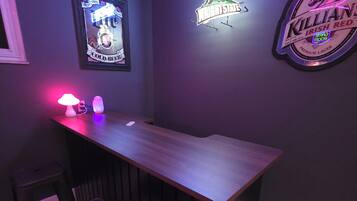 A bar area with a neon sign, a framed poster, and a neon beer logo on the wall.