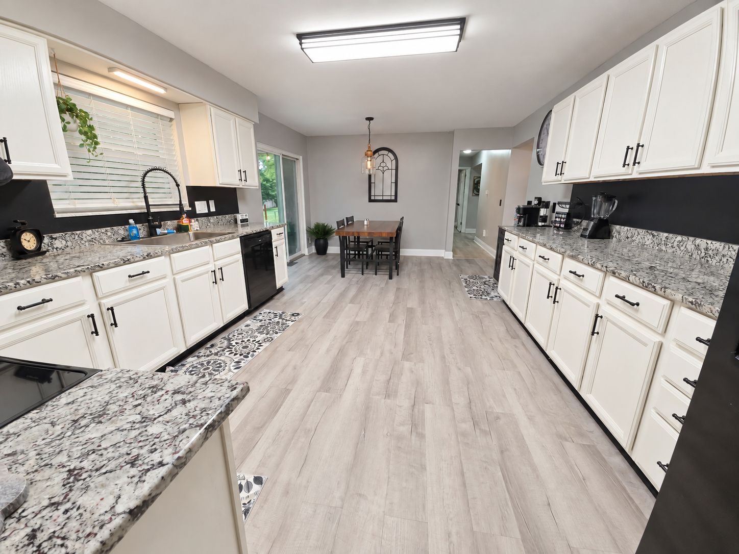 A modern kitchen with white cabinetry, granite countertops, and a dining area with a table and chairs.