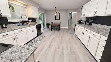A modern kitchen with white cabinetry, granite countertops, and a dining area with a table and chairs.