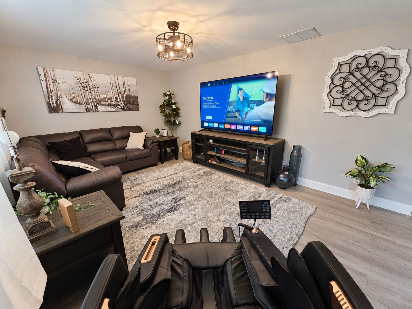 A modern living room with a sofa, a flat-screen TV, a ceiling light fixture, and a decorative wall piece.