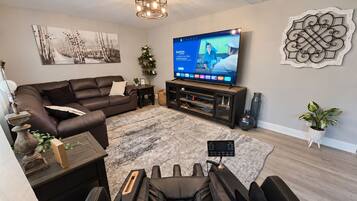 A modern living room with a sofa, a flat-screen TV, a ceiling light fixture, and a decorative wall piece.