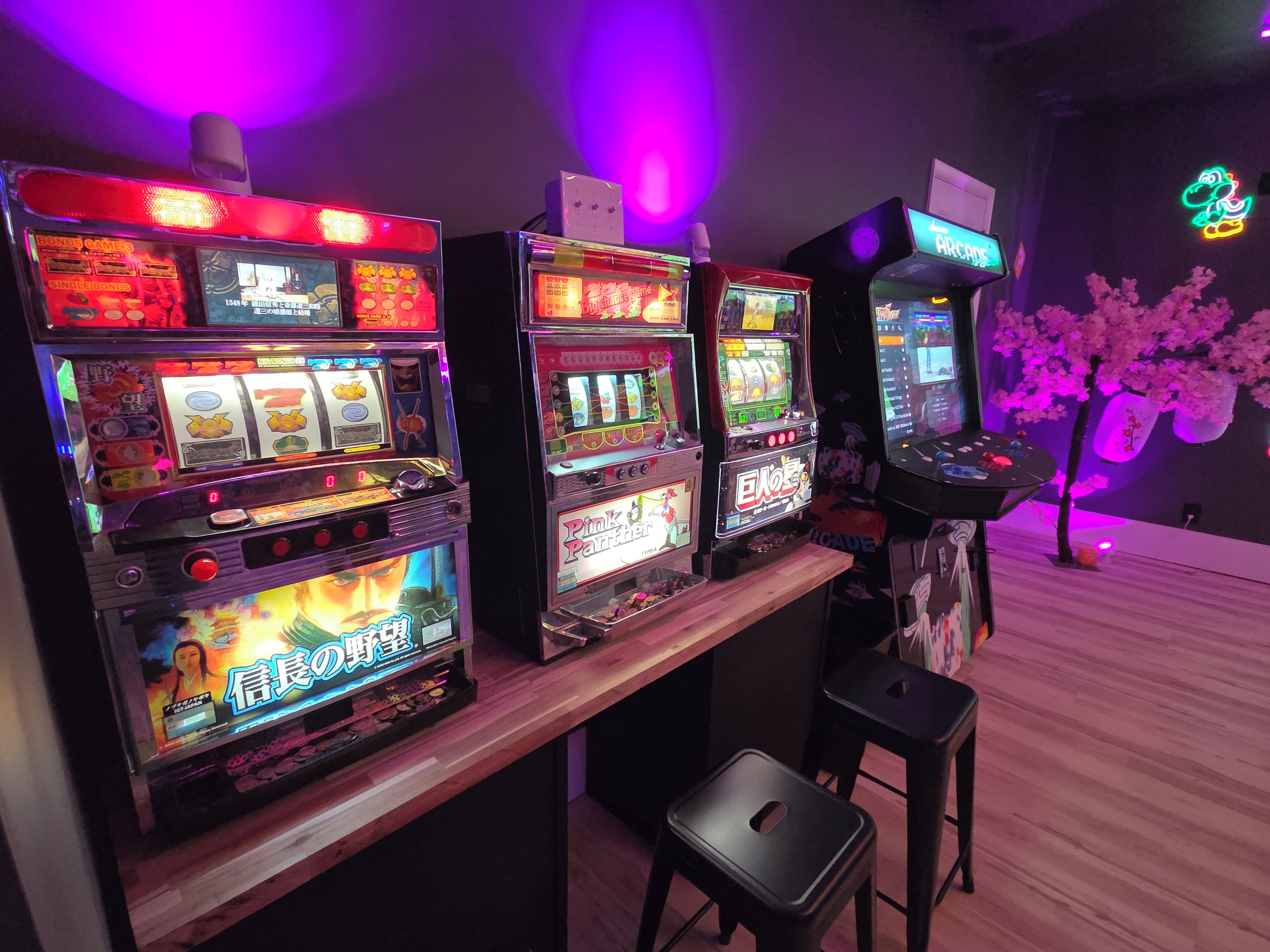 Eine Reihe von Spielautomaten mit japanischen Schriftzeichen, einer Neonreklame und Kirschblüten-Dekorationen.