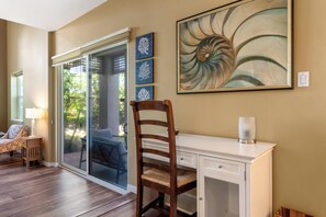Una habitación con un escritorio, una silla, un vidrio que da al exterior y un cuadro en la pared.