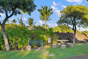 A designated smoking area with a bench and a table surrounded by greenery and trees. - Includes Hilton Pool Pass 2026!  1805 Waikoloa Colony Villas (Waikoloa Beach Resort)