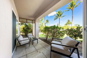 A covered patio with two sofas and a table, overlooking a garden with palm trees and shrubs. - Includes Hilton Pool Pass 2026!  1805 Waikoloa Colony Villas (Waikoloa Beach Resort)