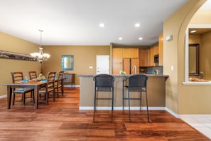 Una cocina moderna con armarios de madera, una isla central con taburetes de bar y un comedor con candelabro.