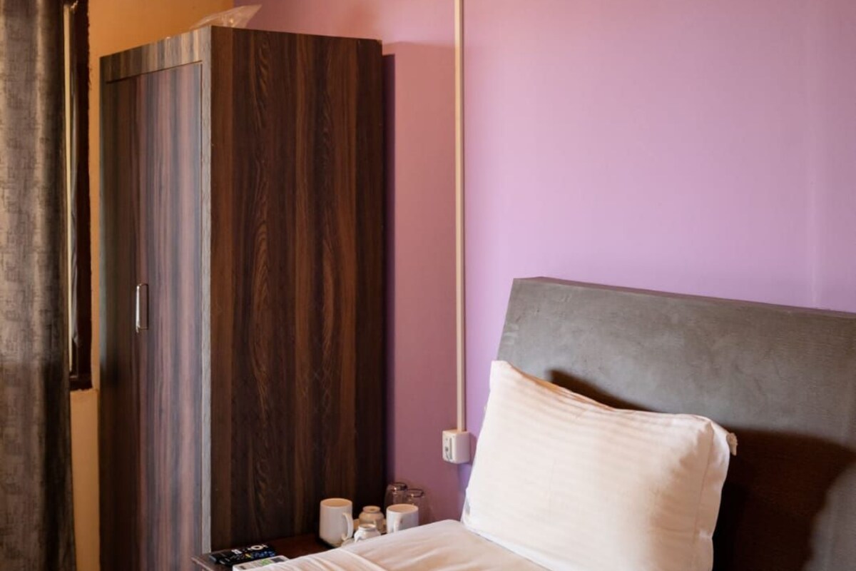 A hotel room with a wooden ceiling, a bed with a grey headboard, and a purple wall.