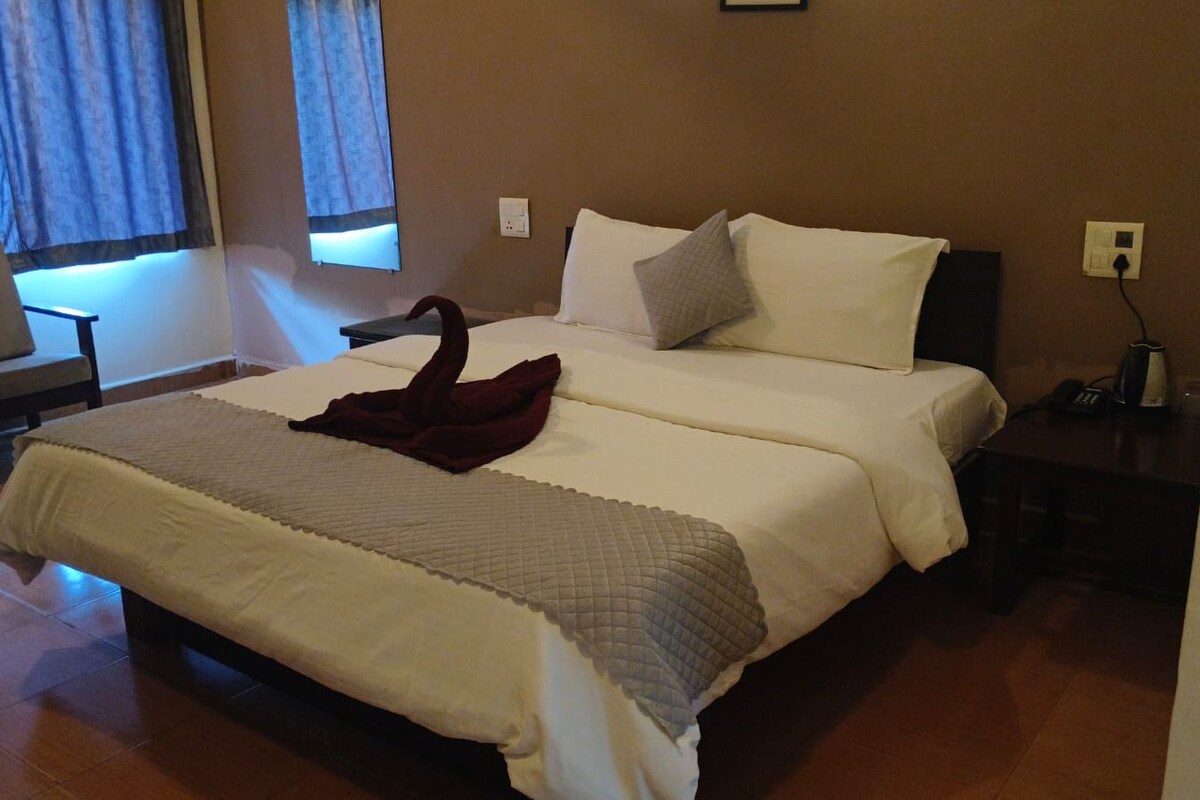 A double bed with a dark throw blanket, a bedside table with a phone, and a chair in a hotel room.