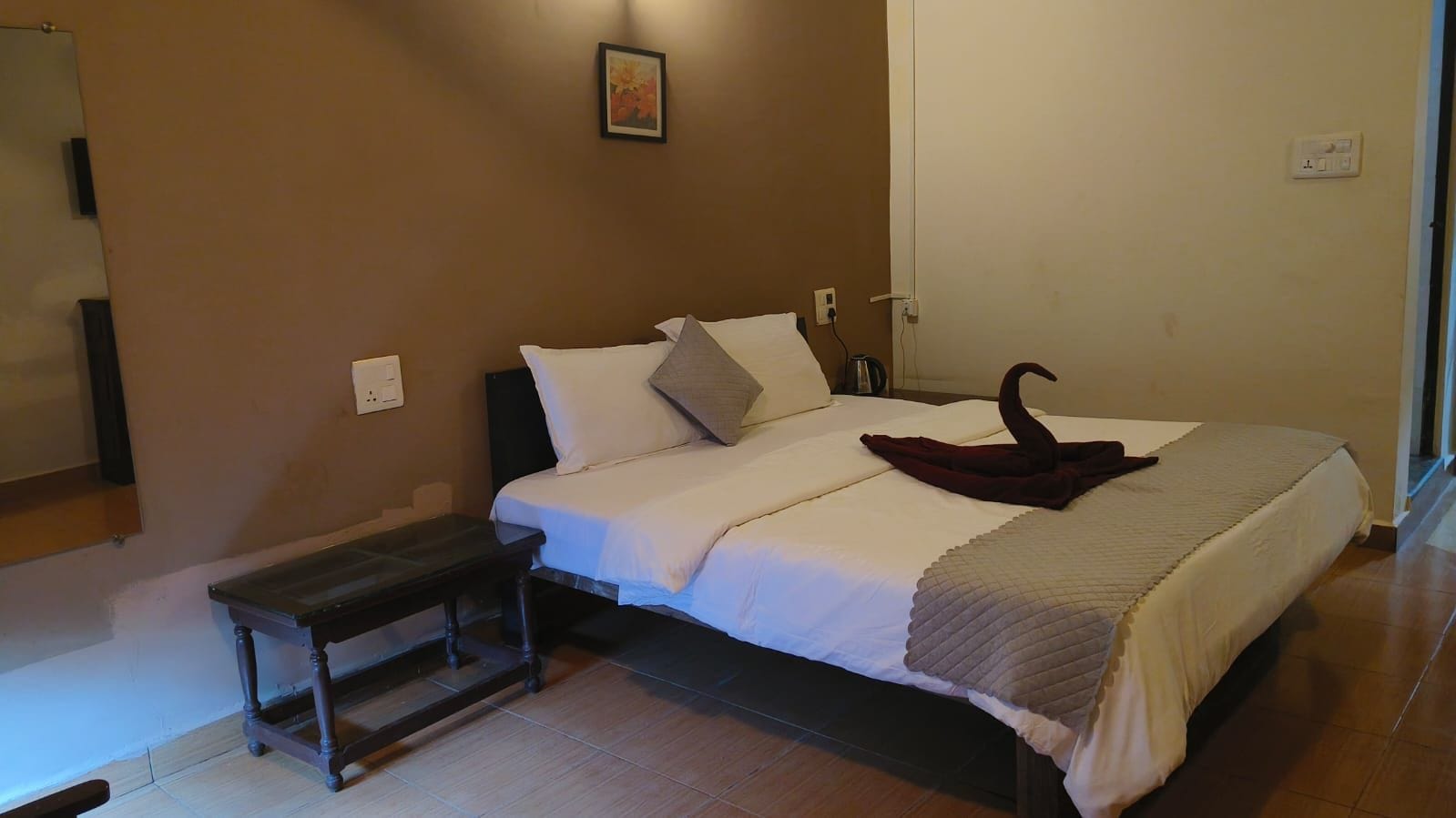 Quarto com cama, um banquinho, uma tomada na parede e um quadro.
