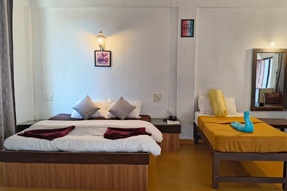 A hotel room with a large bed, a smaller bed, a bedside table, a nightstand, a mirror, and a wall-mounted light fixture.
