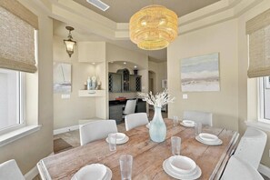 A dining area with a wooden table, white chairs, and a hanging light fixture. - Luxury Flagler Beach Home | Ocean Views | Private Swim Spa | Walk to Beach | 2 King Suites (Flagler Beach)